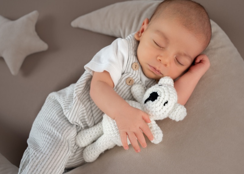 Baby schläft und hält einen gehäkelten Teddy